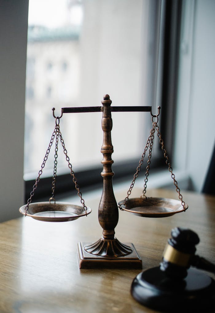 About Decorative judgement scale and gavel placed on desk in light lawyer office against window